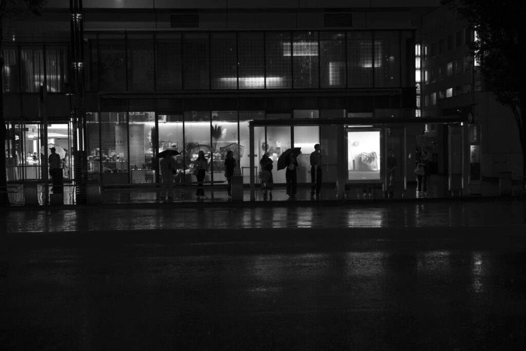 台風の夜、雨の銀座でバス停に並ぶ人々