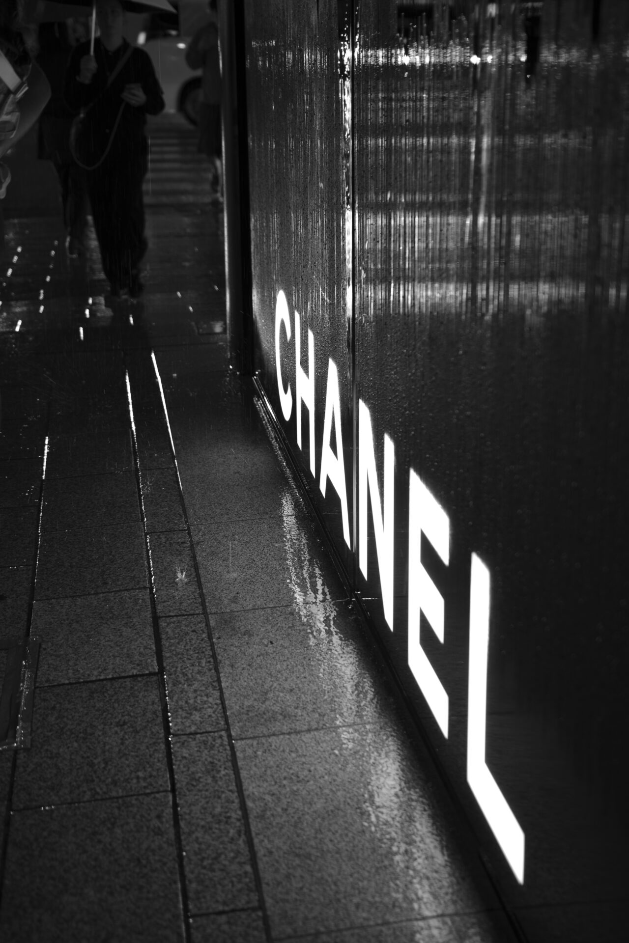 雨に濡れた銀座のCHANEL前を歩く人